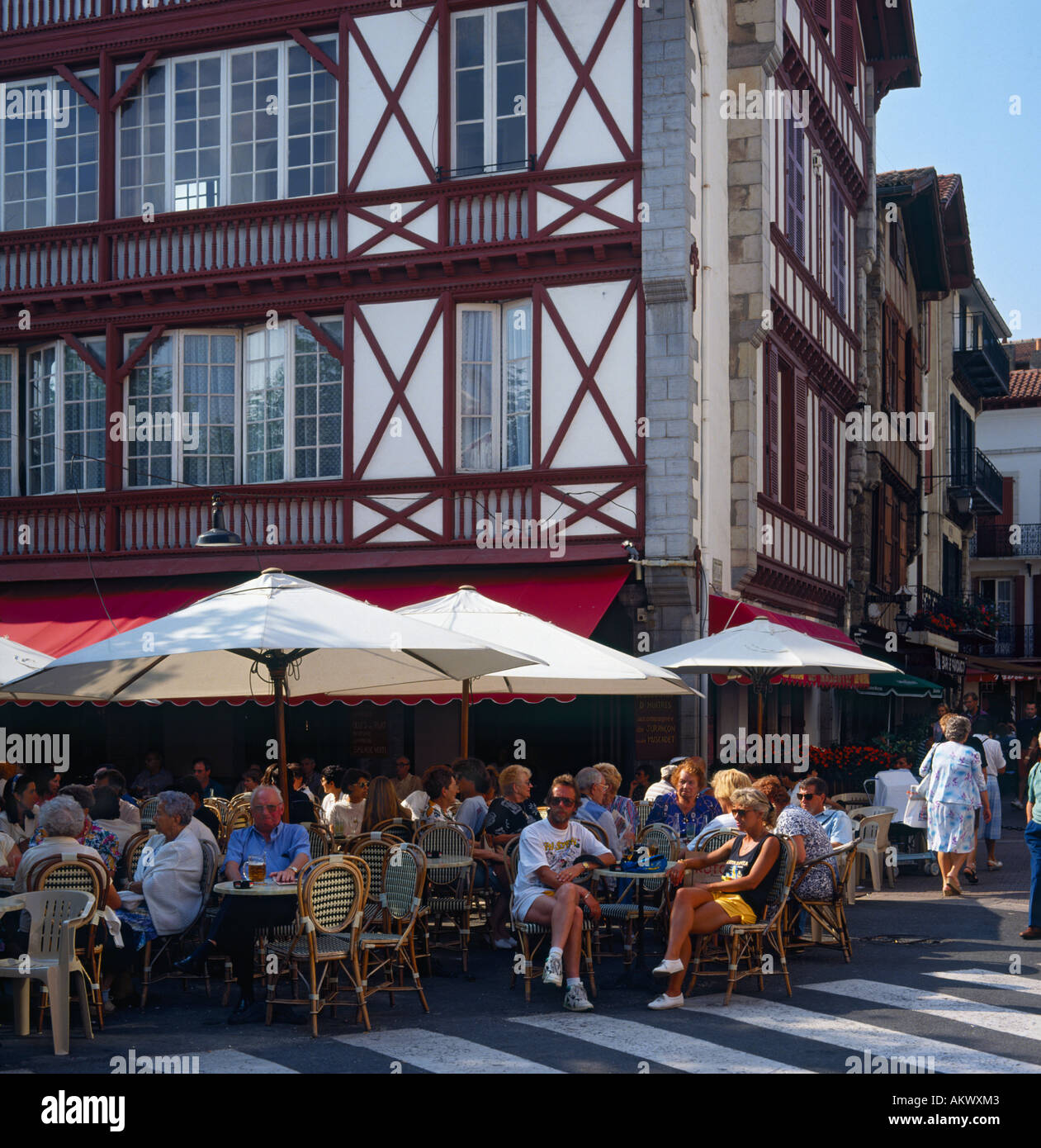 Bianco pietra dipinta la struttura di legno ristorante con persone mangiare fuori sotto gli ombrelloni St Jean de Luz Francia Foto Stock