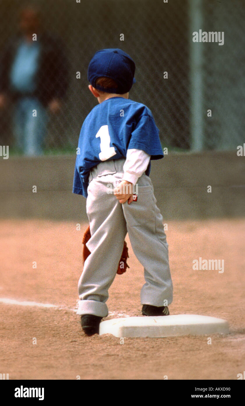 Vista posteriore di un giovane giocatore di baseball in uniforme di graffiare il suo fondo durante una T palla di gioco Foto Stock