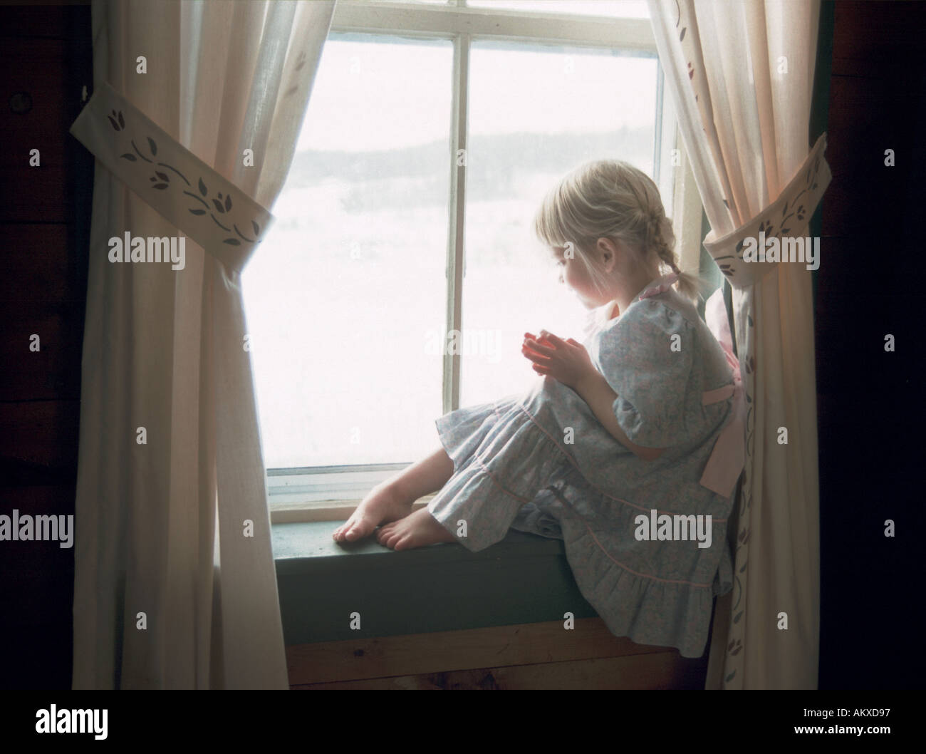 Ragazza in seduta nightgown mediante la finestra Foto Stock