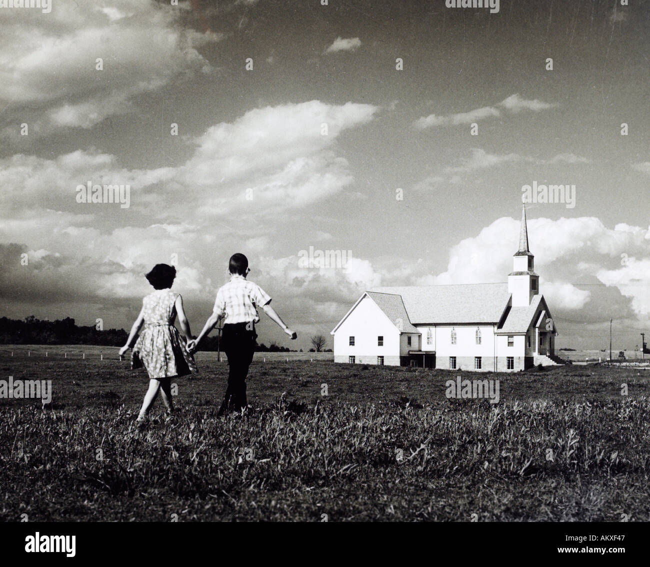 Un ragazzo e una ragazza camminare sul campo verso la chiesa anni cinquanta Foto Stock