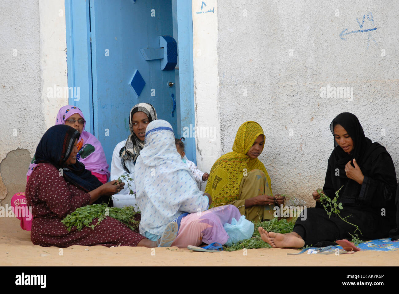 Le donne a sedersi in un villaggio nubiano prima di una porta di entrata e preparare i pasti, Assuan, Aswan, Egitto Foto Stock