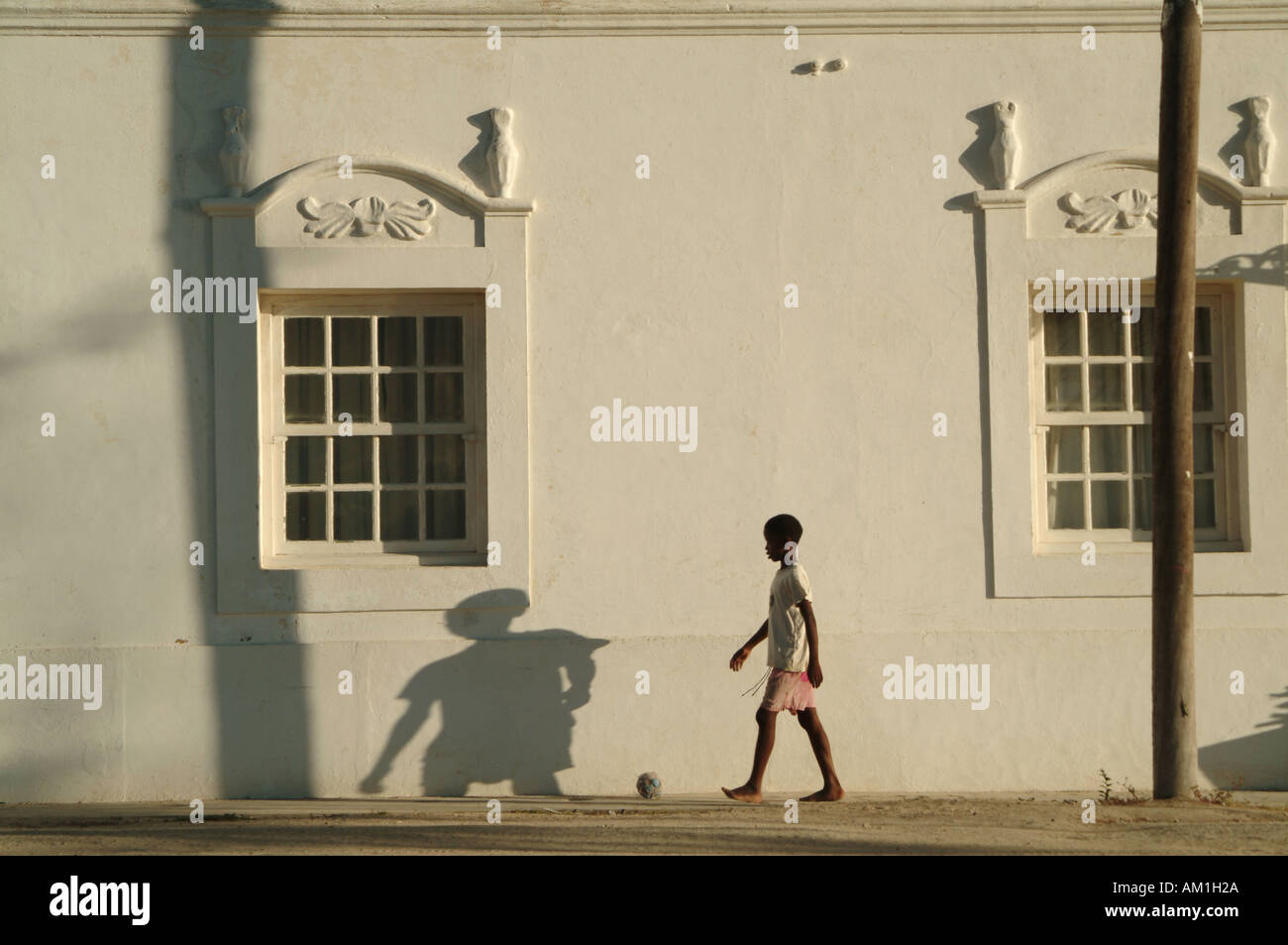 Una gioventù calci un passato di calcio architettura portoghese sulla Ilha de Mocambique, Mozambico, Sud Africa Foto Stock