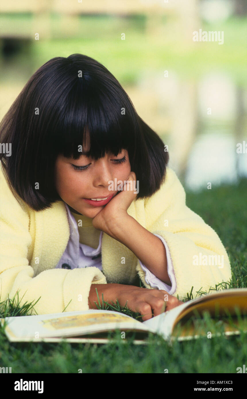 Ragazza distesa sul ventre con mento in mani libro lettura in posizione di parcheggio Foto Stock