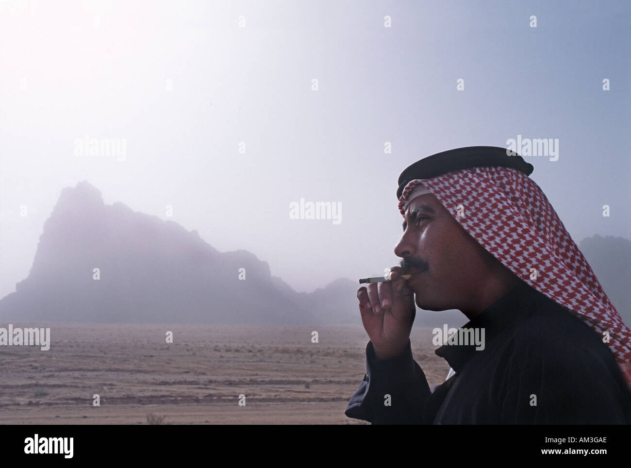 Giordano per uomo che indossa una keffiyah un tradizionale araba velo e fumare una sigaretta Wadi Rum Giordania Foto Stock