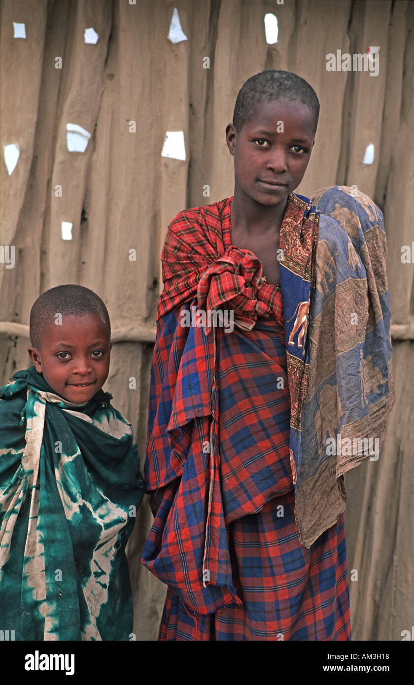Masai bambini avvolti in tessuti colorati in piedi al di fuori del loro fango e legno home N di Arusha in rotta verso S Kenya Tanzania Foto Stock