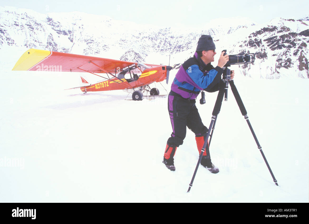 Fotografo Joe Sohm posa con telecamera panoramica durante la ripresa di fronte ad un rosso Super Scout velivolo sul ghiacciaio in Alaska Foto Stock