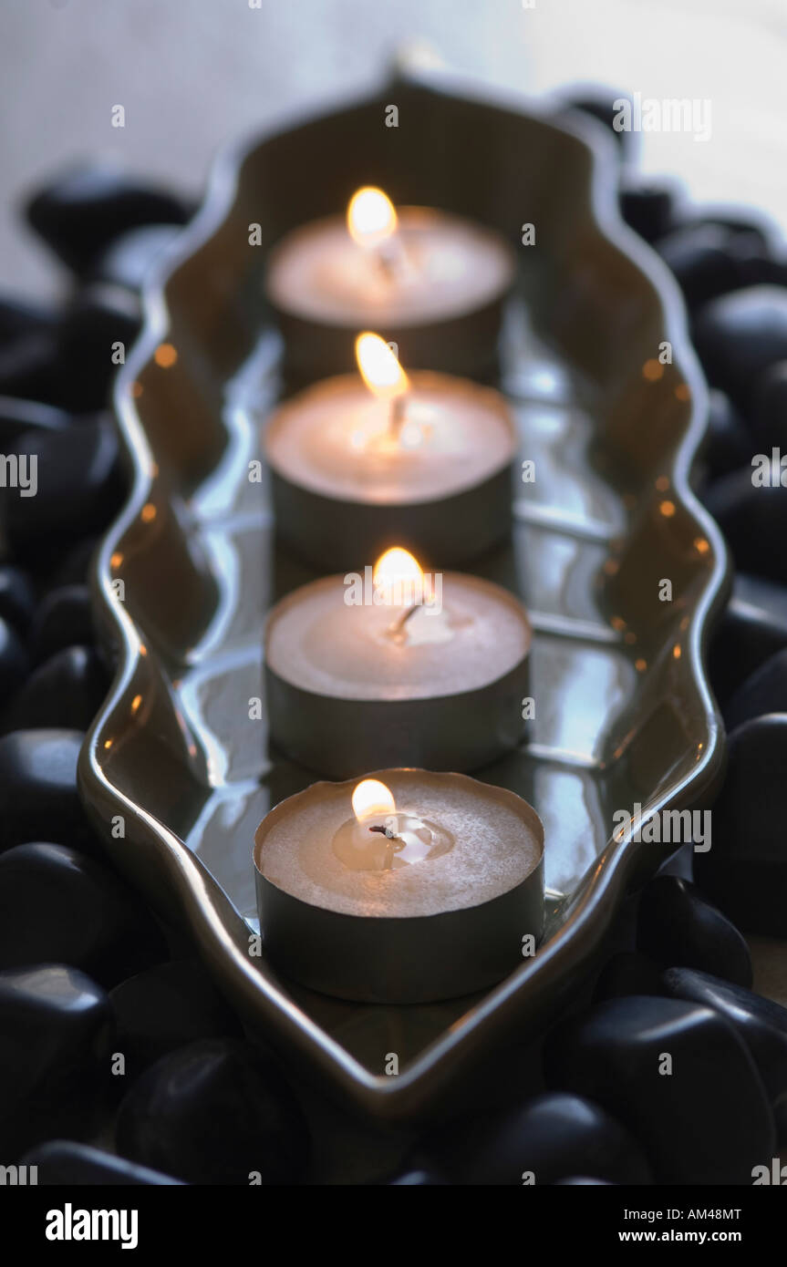 Close-up di quattro aromaterapia candele accese in un vassoio con ciottoli neri Foto Stock