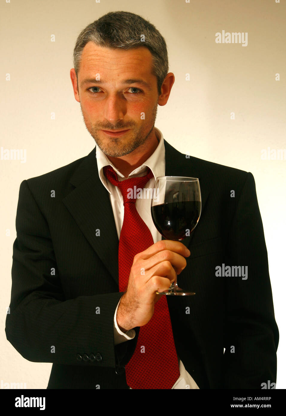Uomo in un vestito e un tirante tiene un bicchiere di vino rosso Foto Stock
