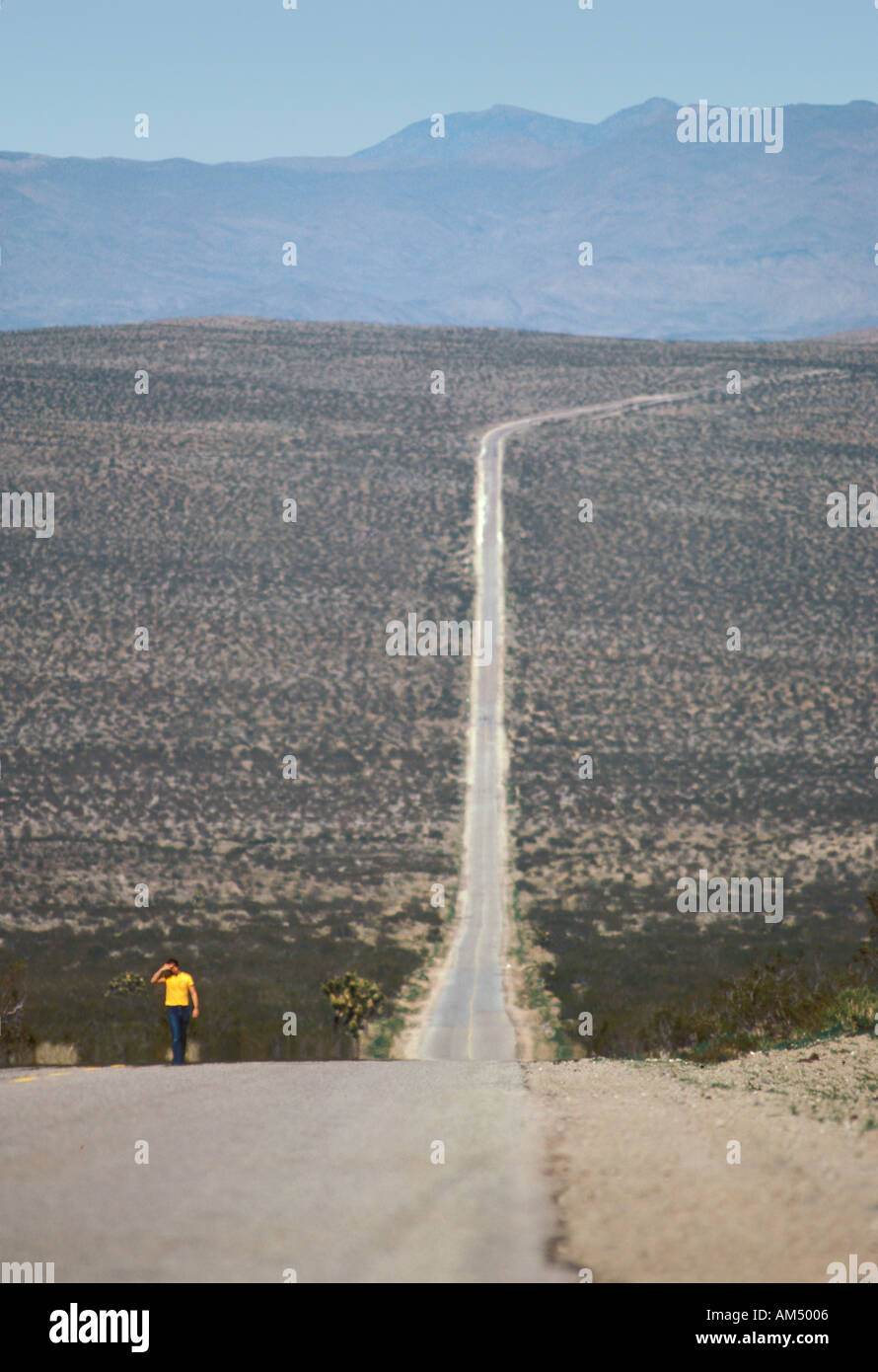 Un uomo solitario passeggiate lungo la lunga strada nel deserto vicino a Death Valley, CA Foto Stock