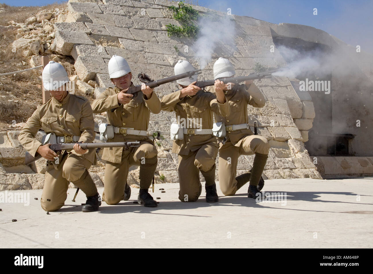 Attori vestiti da soldati in uniforme britannica di epoca coloniale sparano una volley durante una rievocazione storica a Fort Rinella, Malta Foto Stock