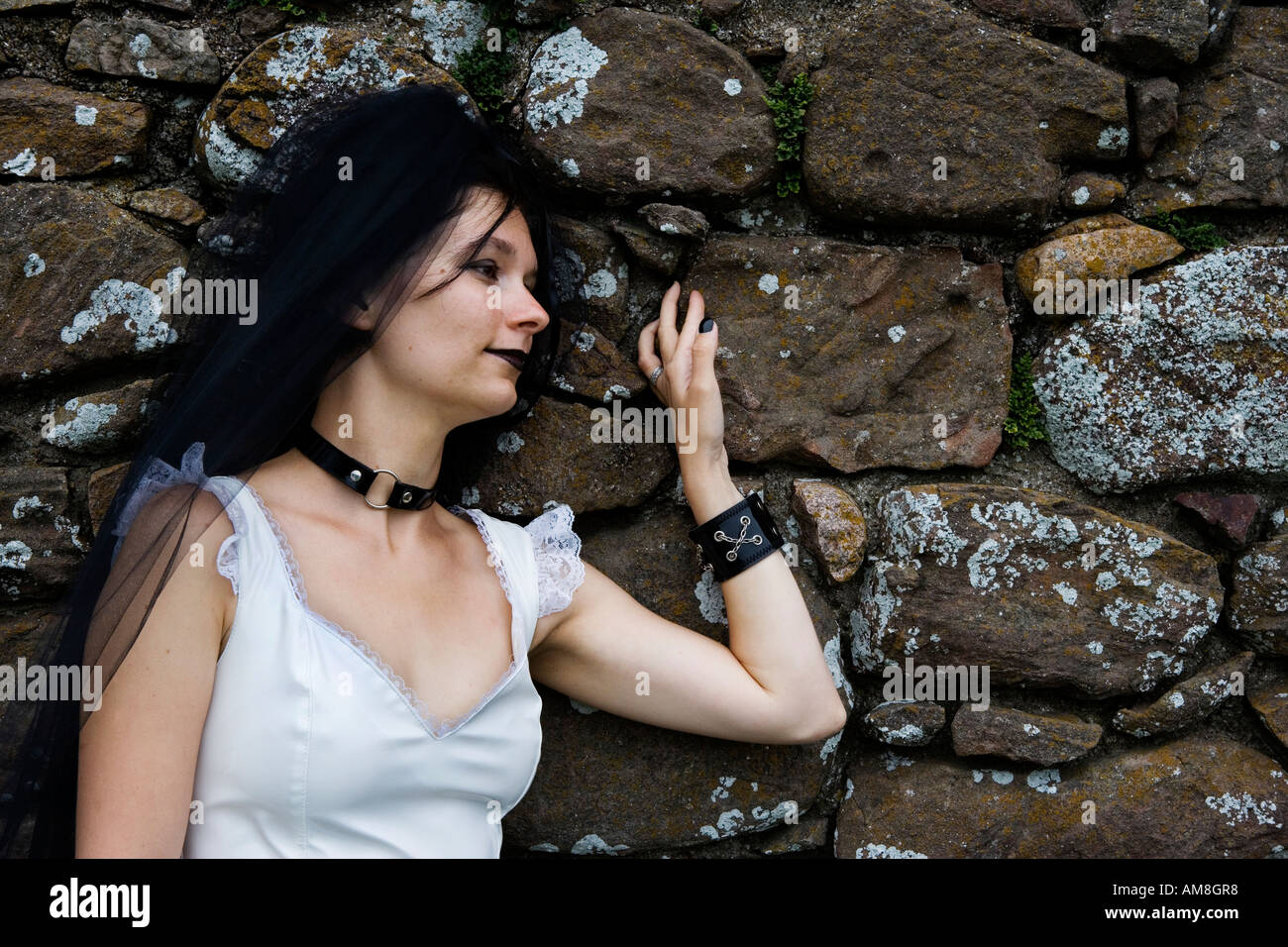 Una singola testa femmina e spalle ritratto con top bianco e il gotico attirew contro un vecchio muro di pietra. Foto Stock