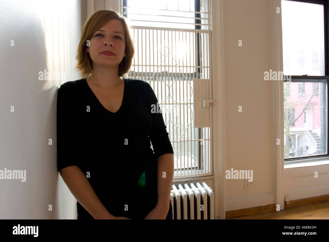 Donna in piedi contro un muro in appartamento vuoto con finestra dietro Foto Stock