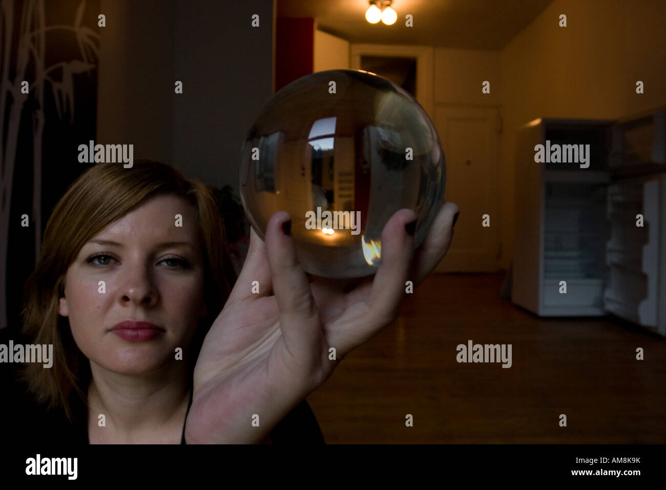 Donna che mantiene una sfera di vetro con la sua immagine rifratti all'interno mentre in piedi in vuoto appartamento di new york Foto Stock