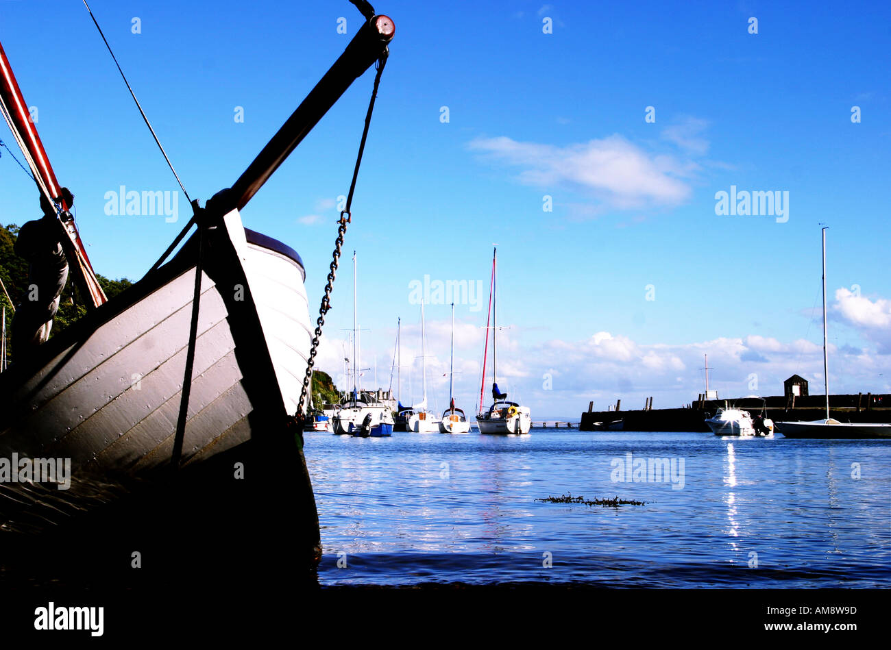 Una piccola barca a vela poggiante sul suo lato sulla spiaggia di aberdour porto con barche a vela in background fife Scozia 20 Foto Stock