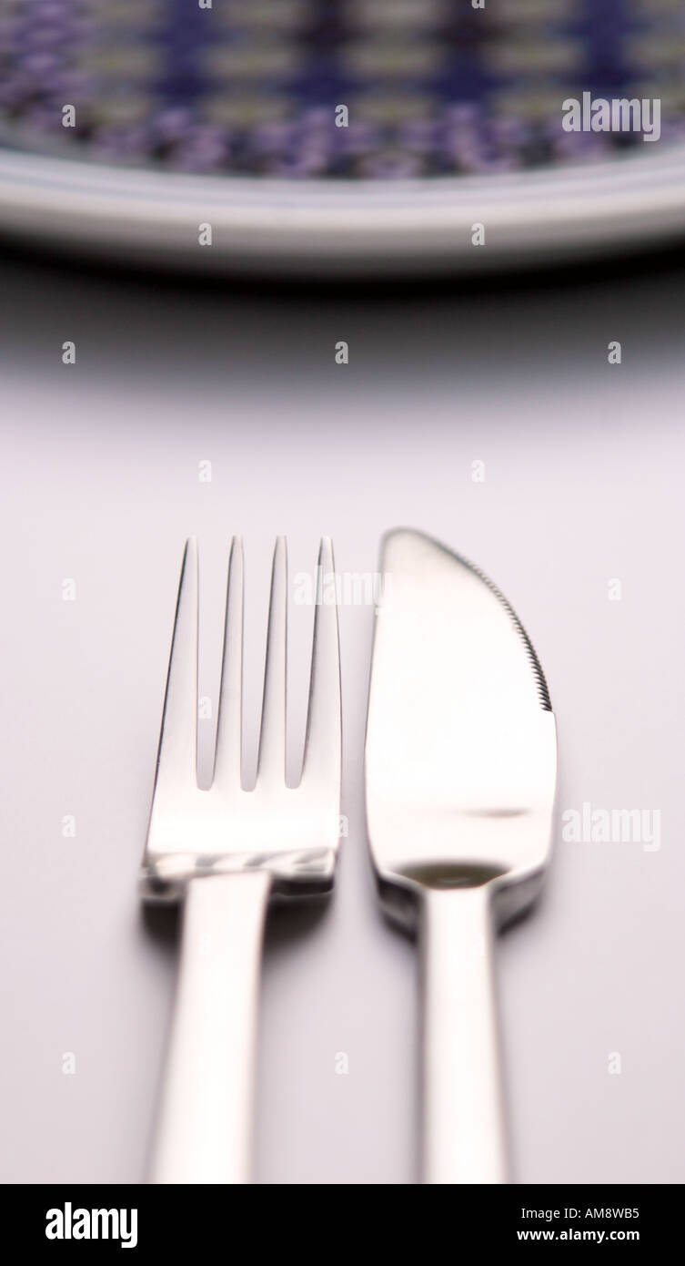 Immagine astratta di un coltello e forchetta affiancati su una superficie bianca con il bordo curvo di una piastra di sommità del imag Foto Stock