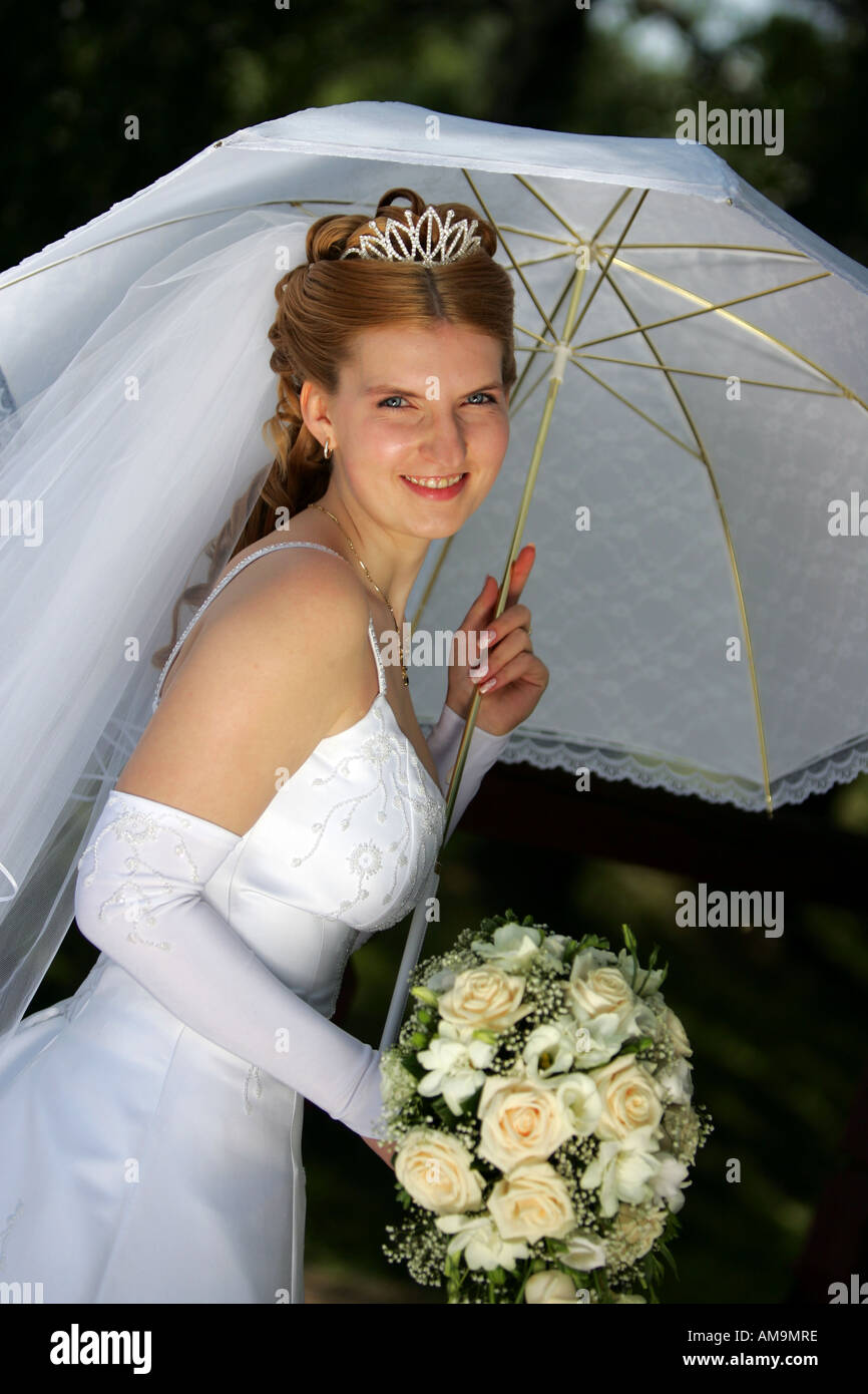 Un ritratto di una sposa in bianco di un abito da sposa con un bouquet. Ella è in piedi sotto un ombrello. Foto Stock