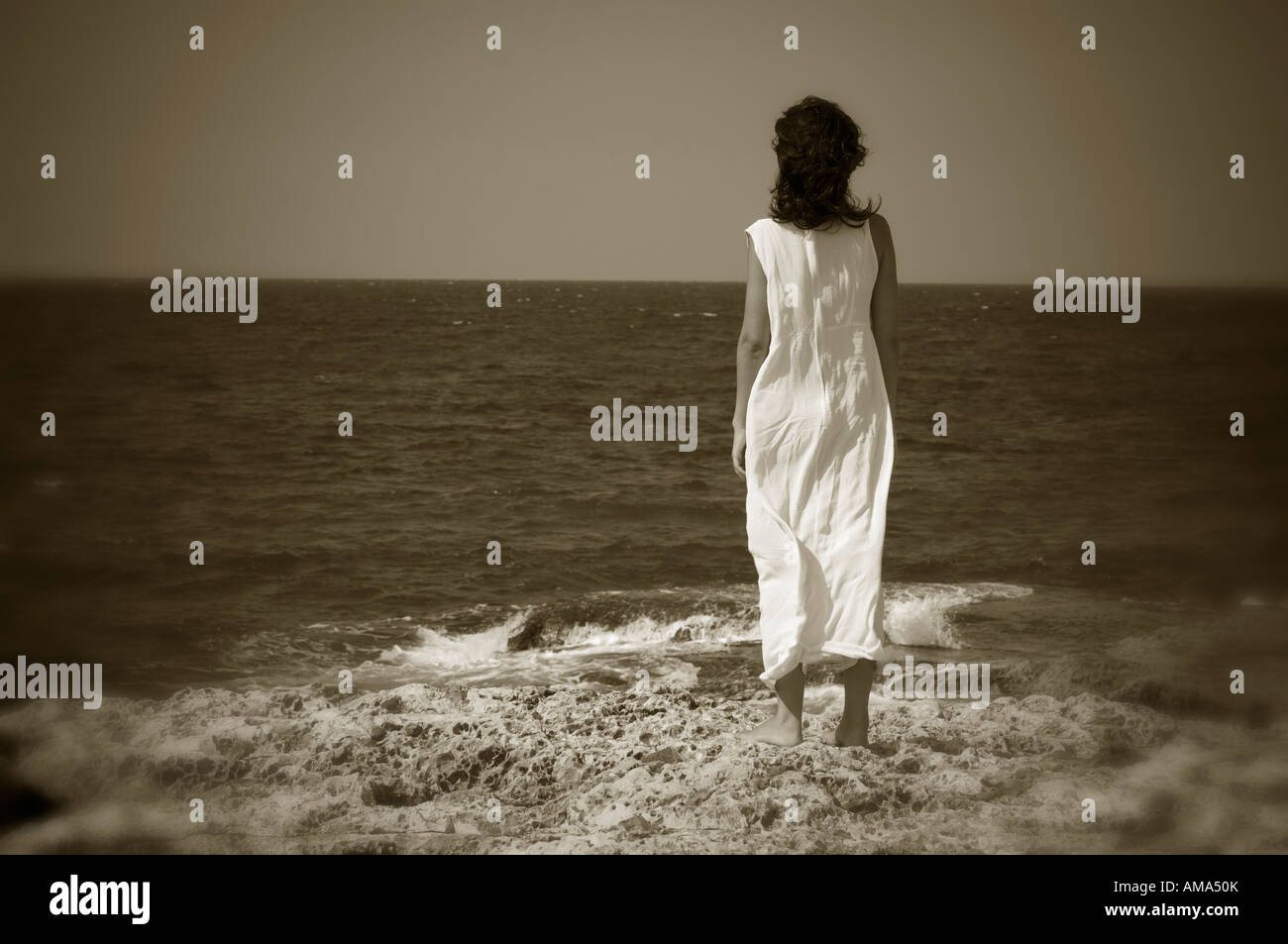 Moody immagine atmosferica con una rara vista di una bruna in abito bianco in piedi vicino al mare Foto Stock