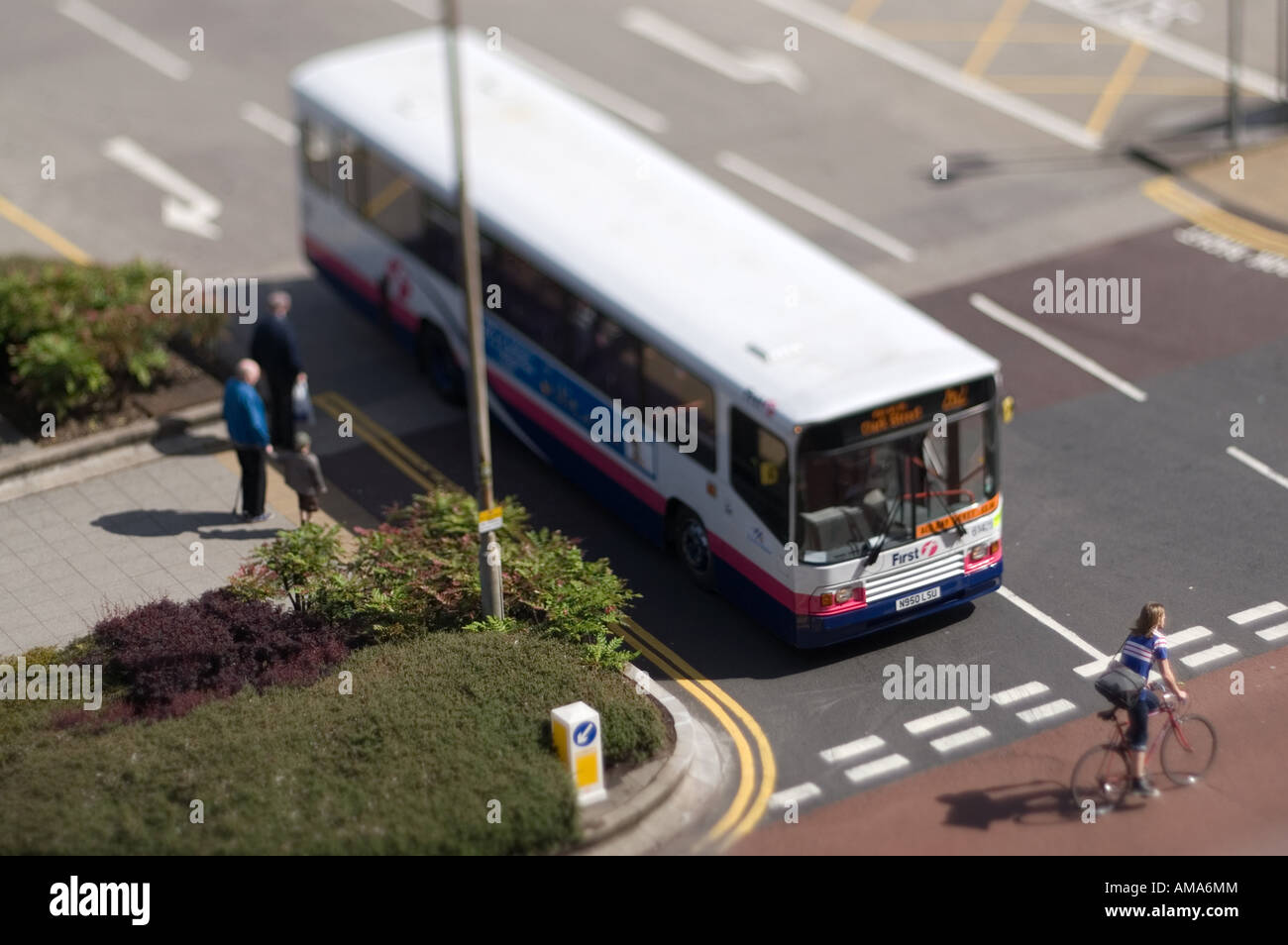 Tilt-shift ciclista passando davanti ad un bus - i pedoni a guardare. Foto Stock