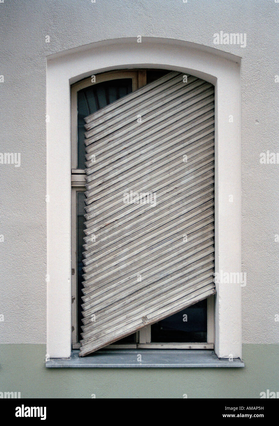 Un otturatore rotto appeso ad angolo inclinato su una finestra Foto Stock