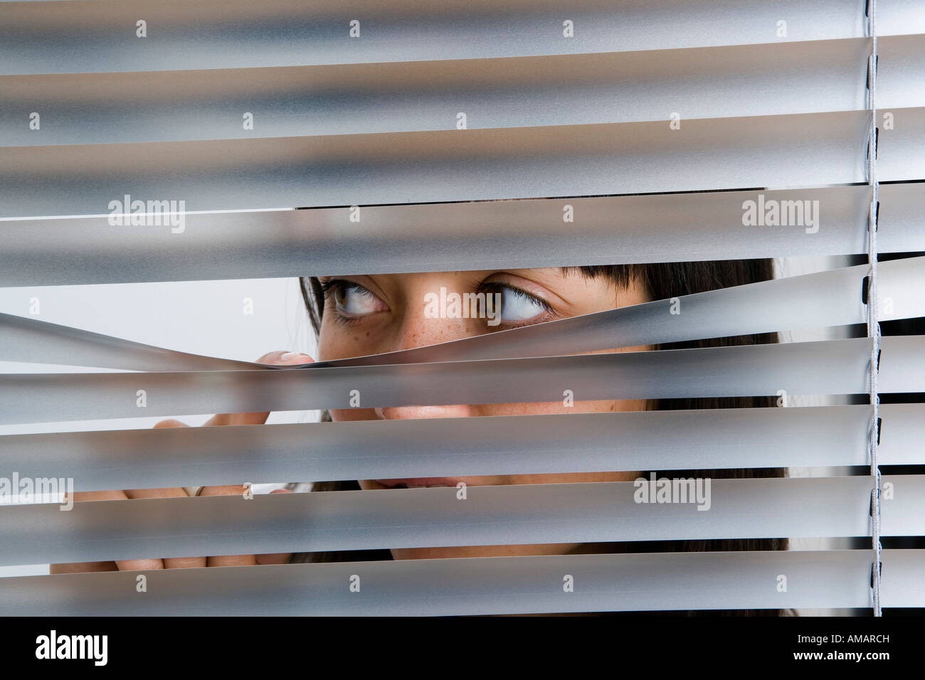 Una giovane donna del peering attraverso le veneziane Foto Stock