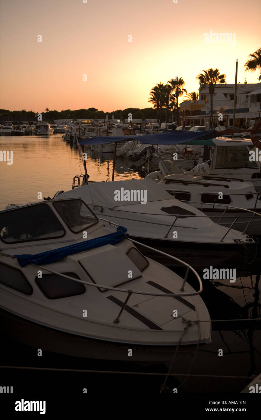 Silhouette tranquillo come il sole tramonta su barche ormeggiate nel porto di Cala d'en Bosch, Minorca, Isole Baleari, Spagna. Foto Stock