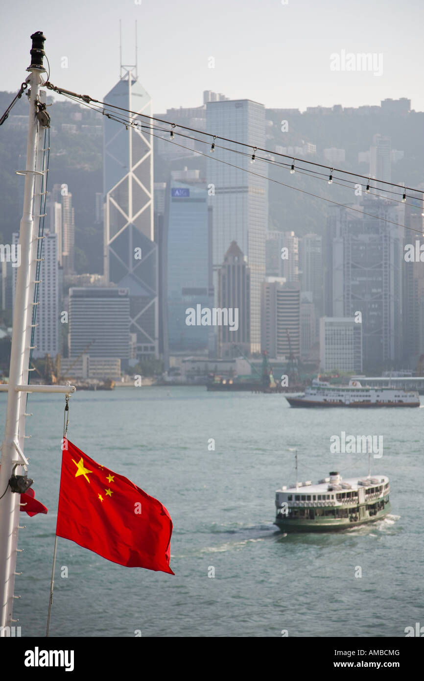 La bandiera nazionale cinese vola dal montante di una nave da crociera ormeggiata nel porto di Hong Kong, con l'isola sullo sfondo. Foto Stock