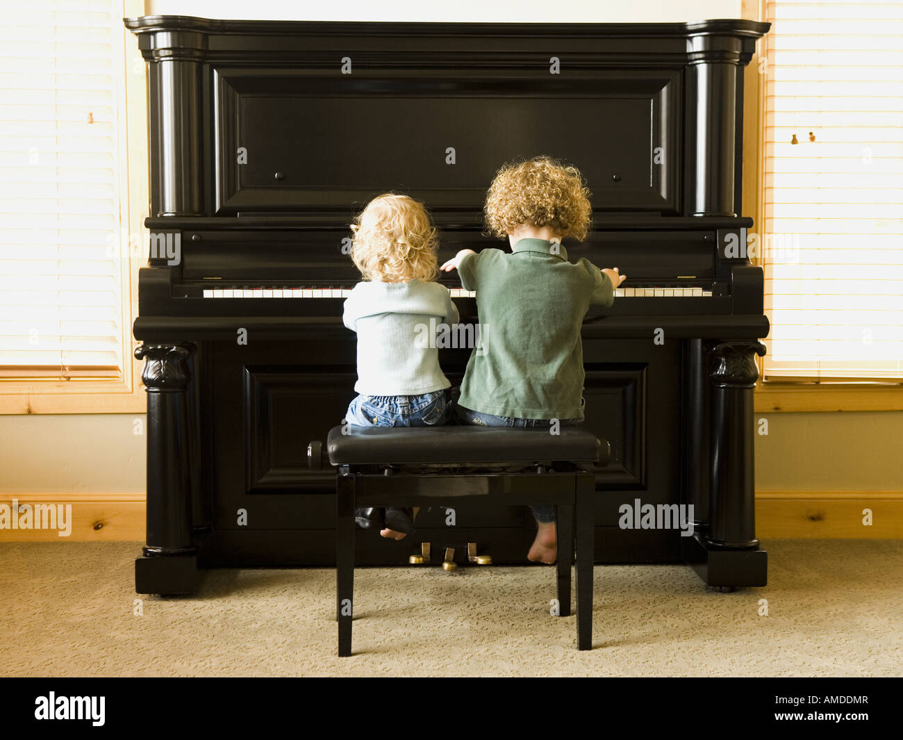 Vista posteriore di due bambini seduti al pianoforte verticale Foto Stock