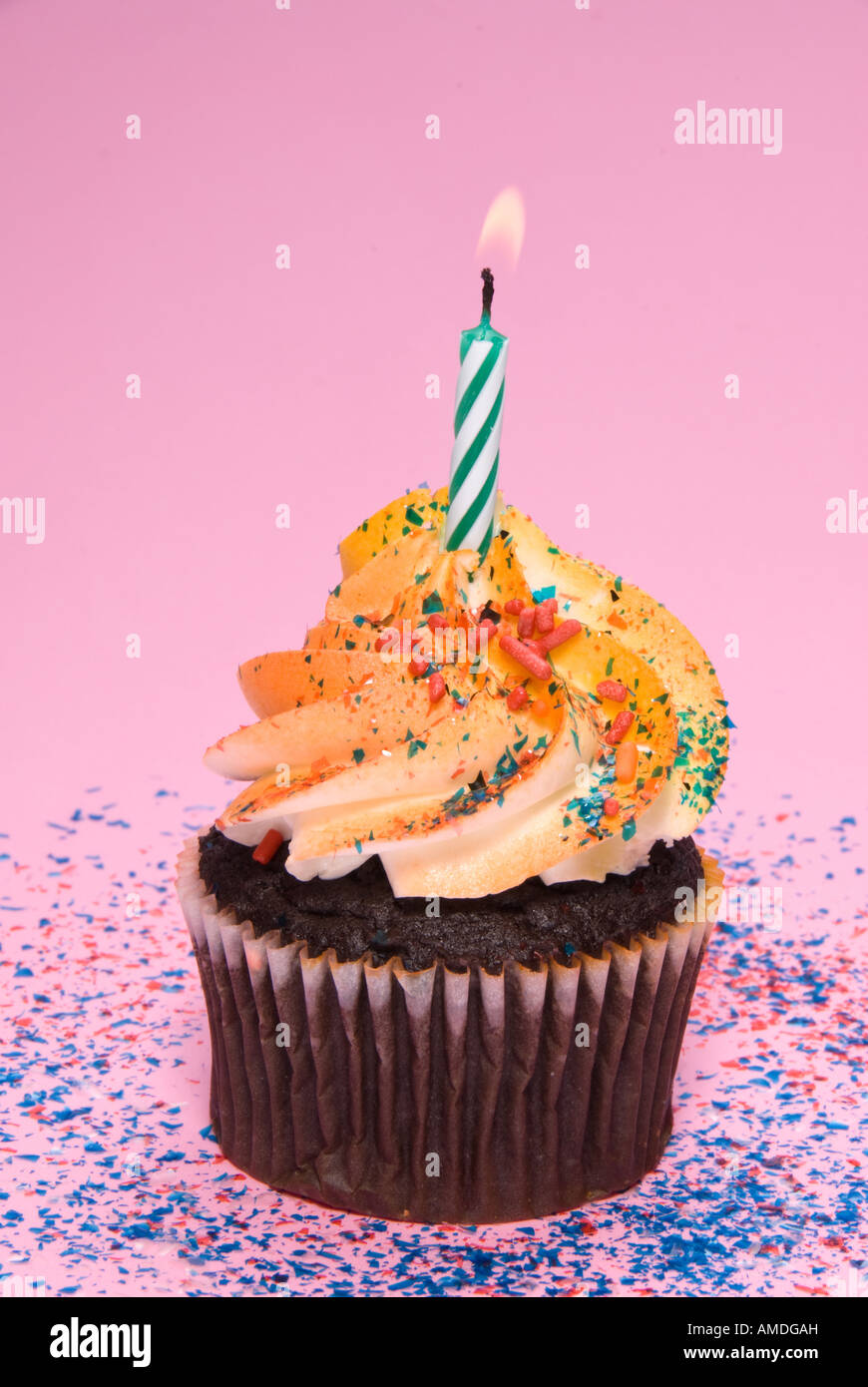 Un delizioso cioccolato tortina con una candela accesa e colorata glassa e spruzza su una rosa di zucchero di sfondo coriandoli Foto Stock