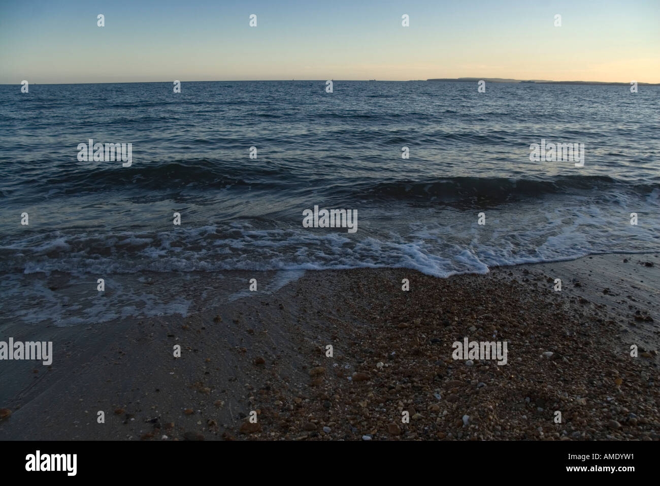 Piccole onde che si infrangono sulla sabbia e ciottoli spiaggia al tramonto Foto Stock