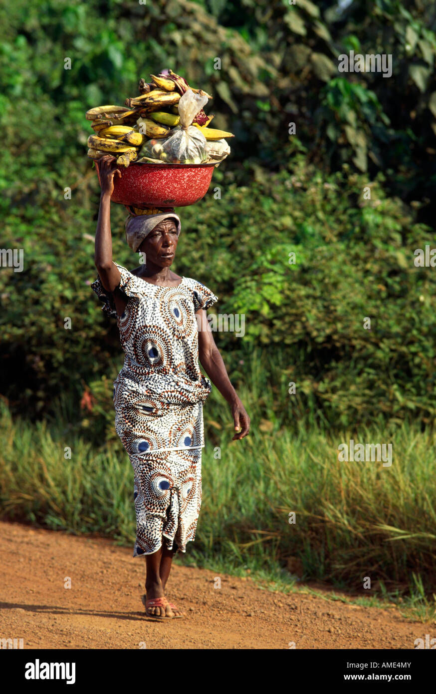 Una donna in abito tradizionale di passeggiate in città con la produzione di equilibrato sul suo capo il giorno di mercato Tabou Africa occidentale Foto Stock