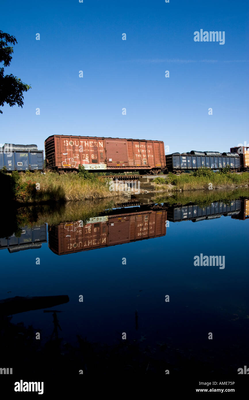 Treno merci rotola lungo la calma acqua con una vivace riflessione Foto Stock