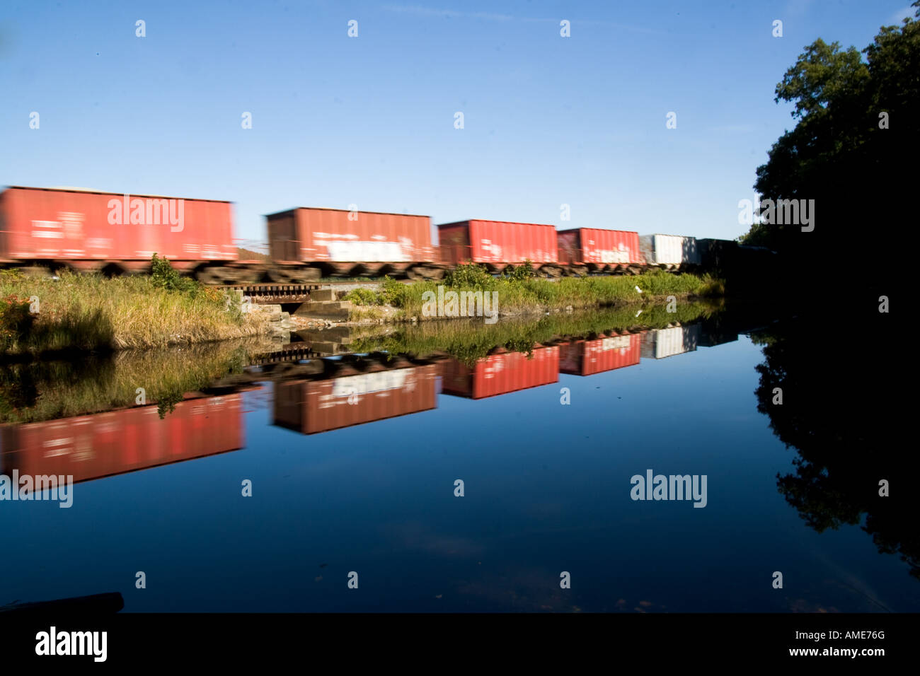 Treno merci rotola lungo la calma acqua con una vivace riflessione Foto Stock