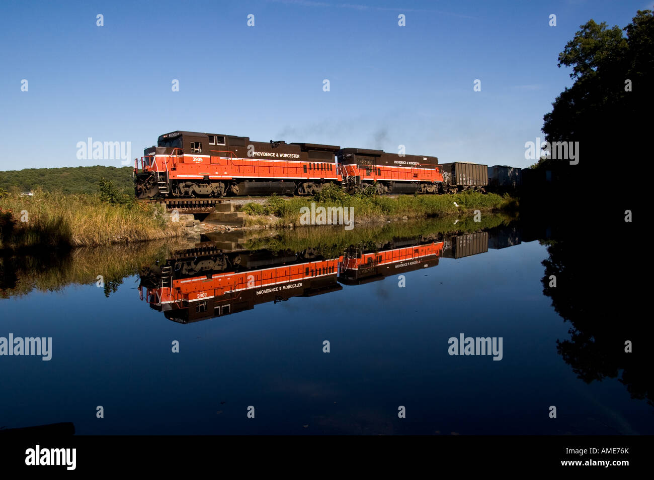 Una Provvidenza & Worcester Railroad (PW) treno merci rotola lungo la calma acqua con una vivace riflessione Foto Stock