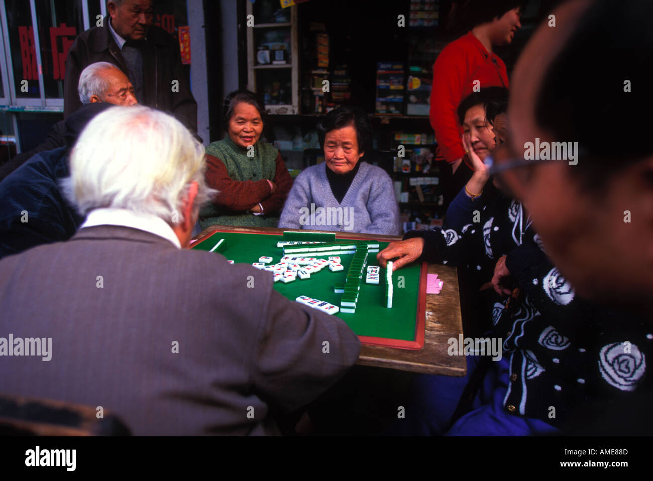 Quattro pensionati cinesi si riuniscono intorno a un tavolo mahjong, impegnandosi in un gioco tradizionale basato su piastrelle, godendosi il tempo libero e il cameratismo culturale. Foto Stock