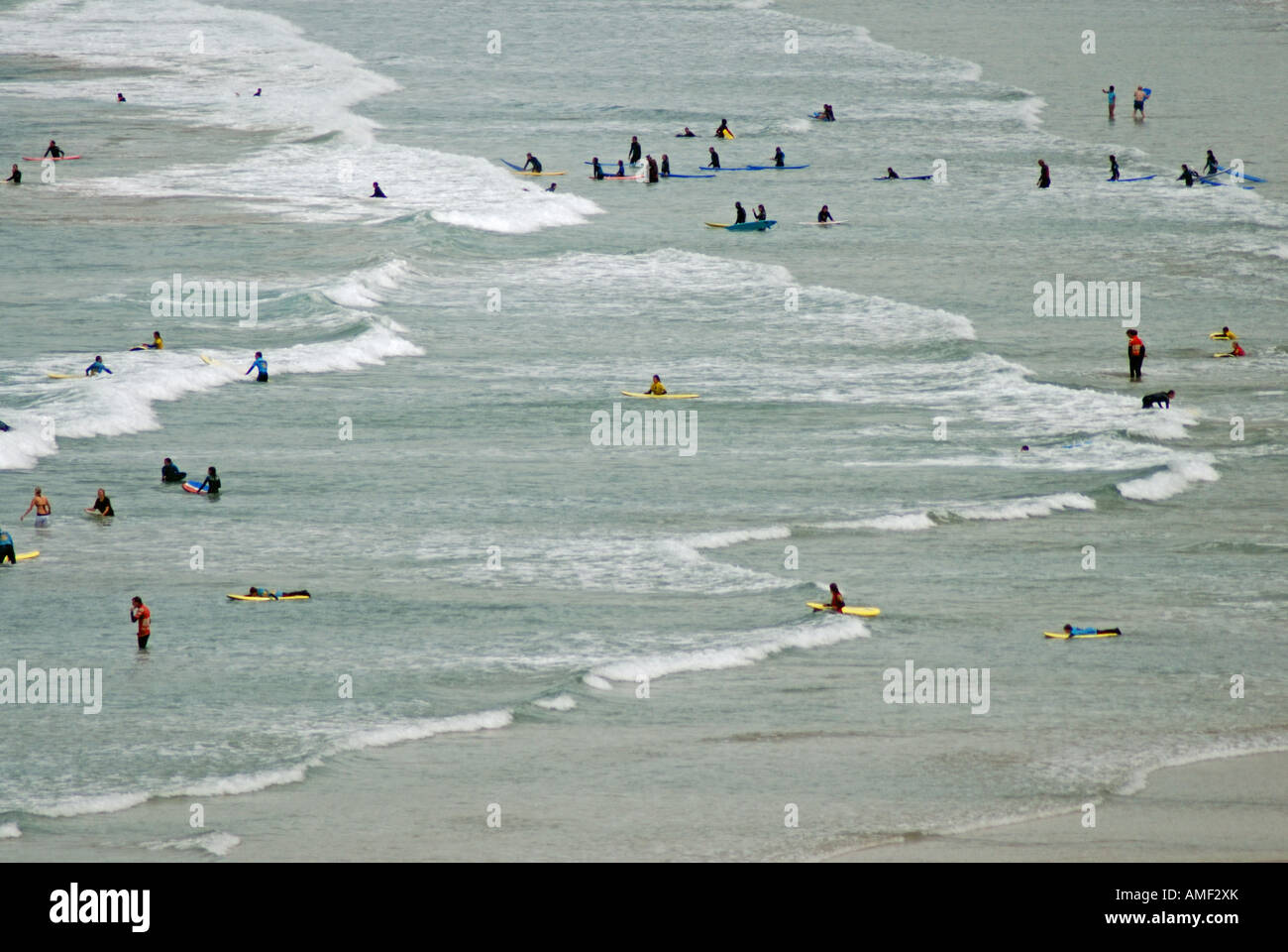 Diversi Cornish surfers in attesa sul mare si gonfiano come bianco onde si infrangono sulla spiaggia aperta Foto Stock