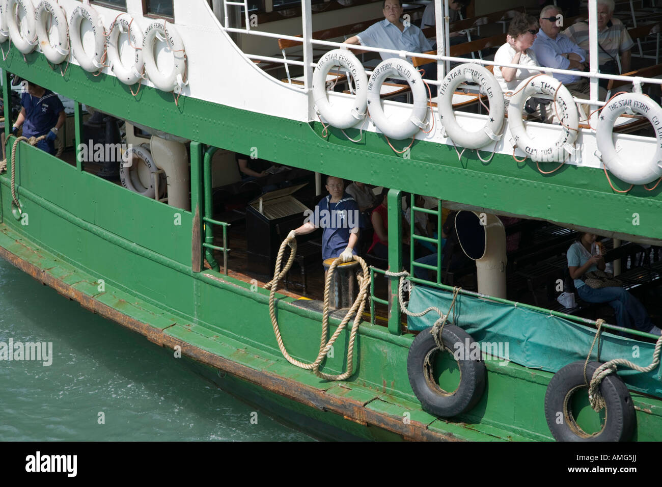 Un marinaio su una delle Star Ferries si prepara a lanciare una cima di ormeggio a un collega sul molo come il traghetto approda a Kowloon Foto Stock
