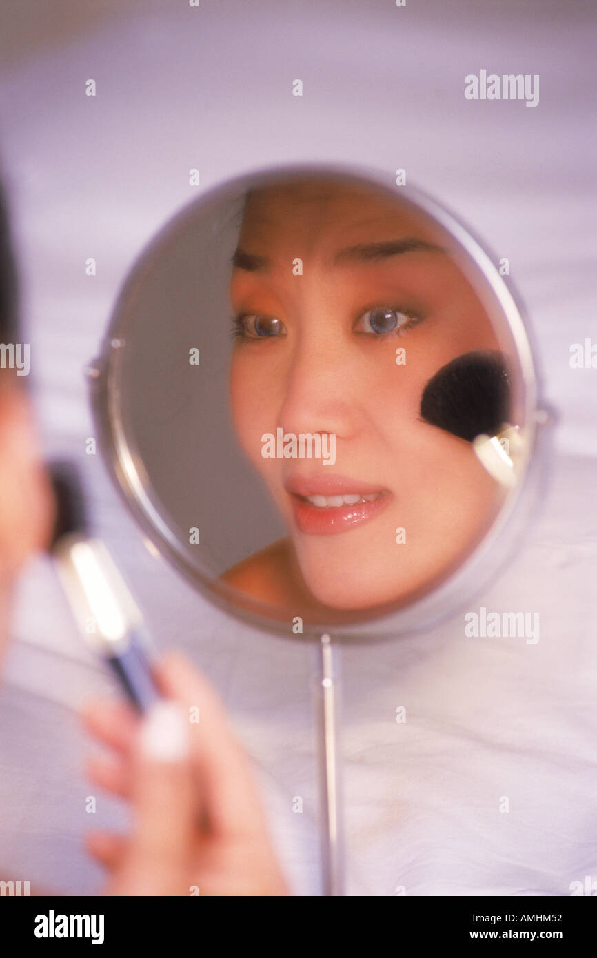 Donna asiatica di applicare il make up utilizzando pennello e piccolo specchio Foto Stock