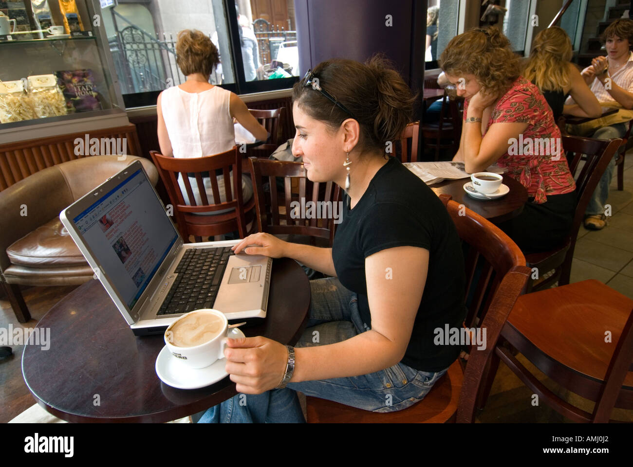 Giovane donna navigando in internet su un computer portatile in un caffè nero, London, England, Regno Unito Foto Stock