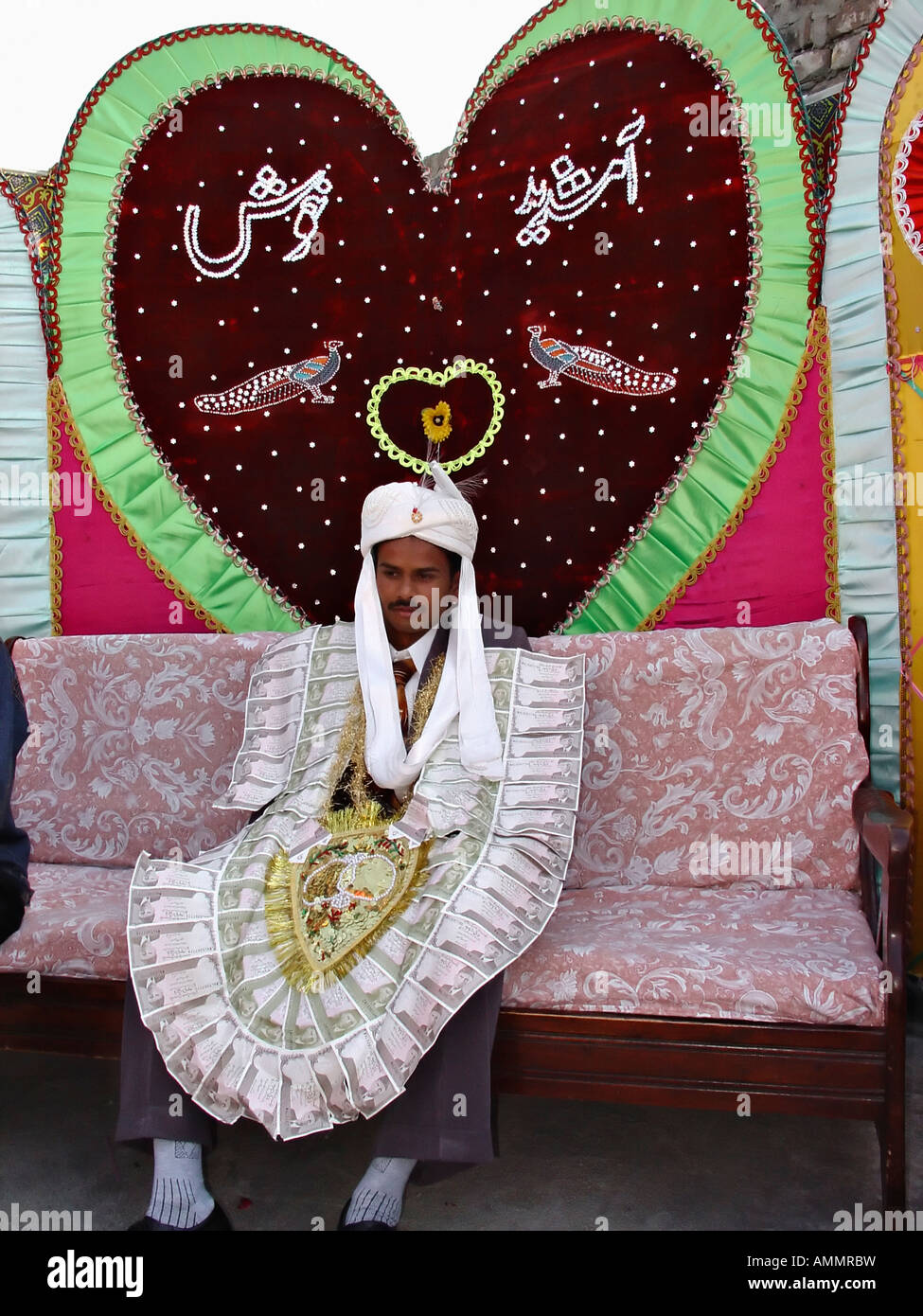 Nozze cristiane in Pakistan per lo sposo siede sotto forma di cuore decorazione indossando un dono fatto di rupee note Foto Stock