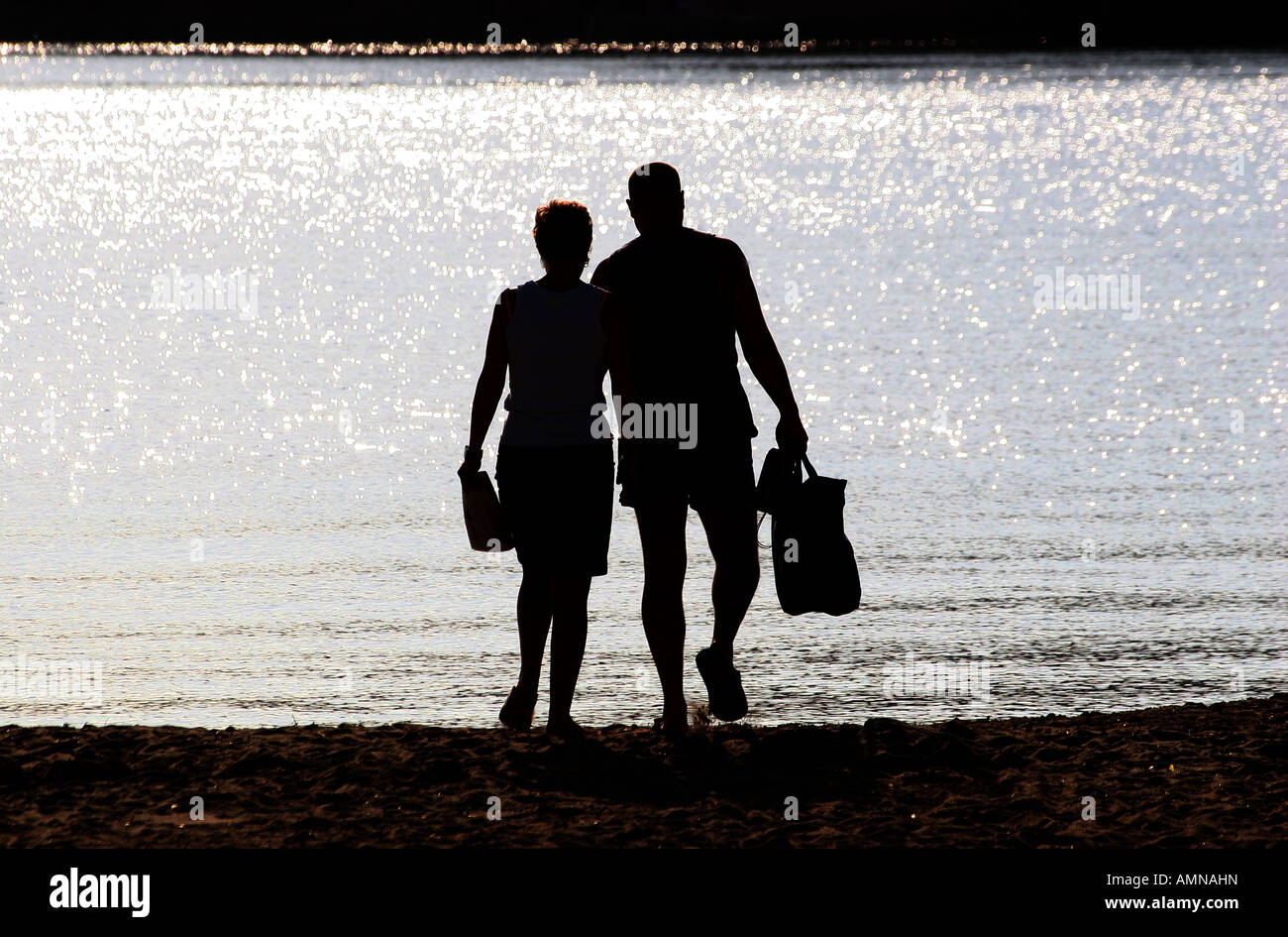 La silhouette di un uomo e di una donna che cammina lungo la sabbia a bordo del mare in bright early morning sun in Maiorca. Foto Stock