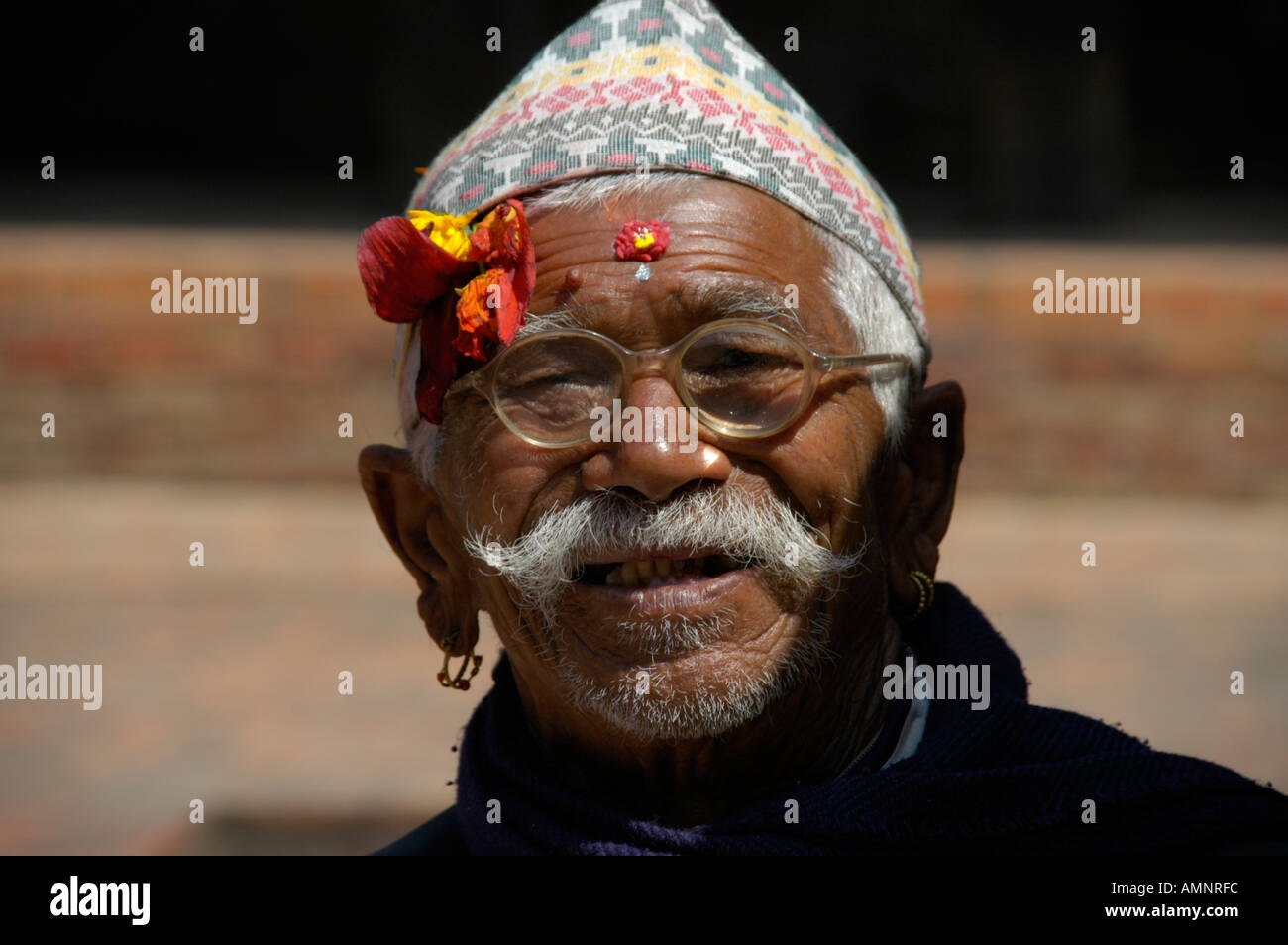 Ritratto uomo Newari con tradizionale hat e fiore sulla sua fronte indossando occhiali Bhaktapur Nepal Foto Stock