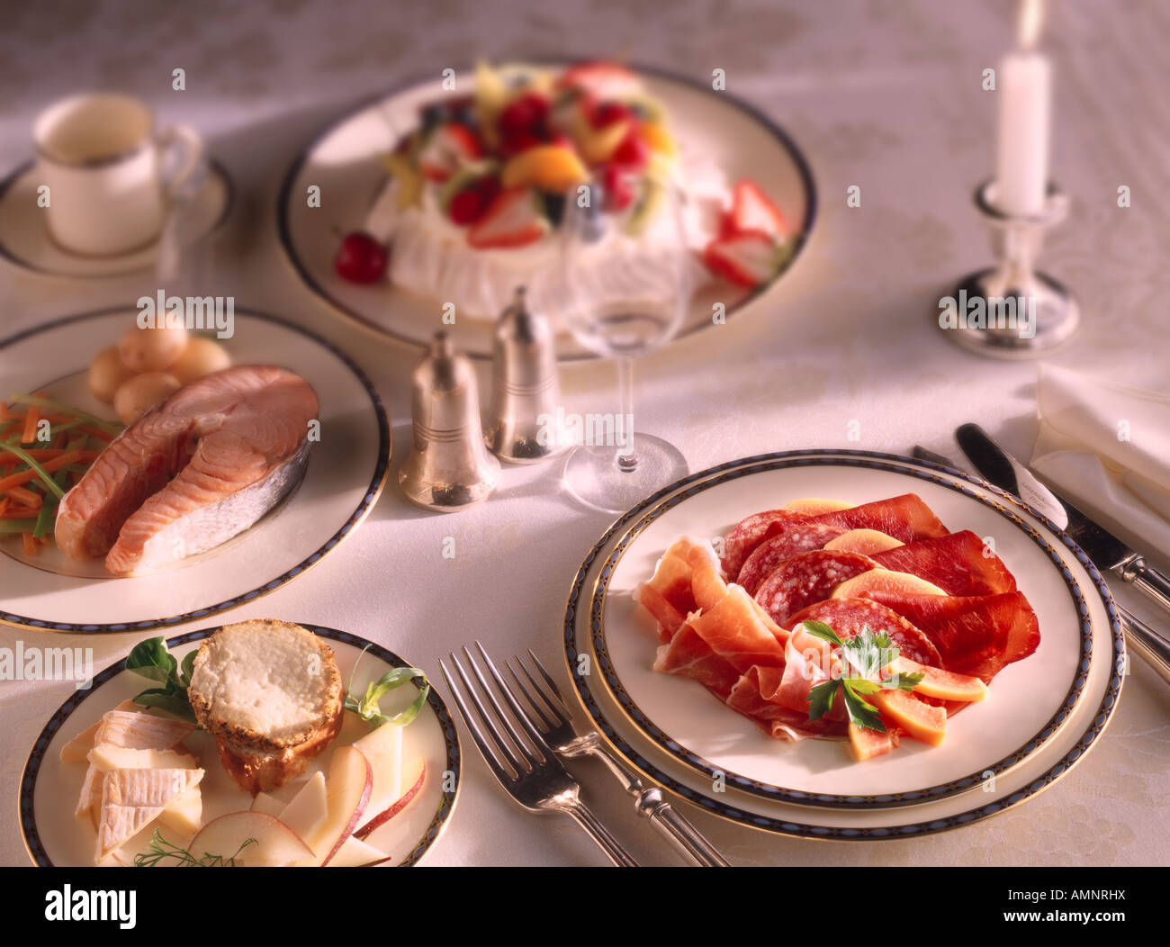 Un pasto completo di starter Charcutterie, corso principale, bistecca di salmone, Dessert Pavlova. Una cena o un pranzo impostazione su un tavolo. Foto Stock