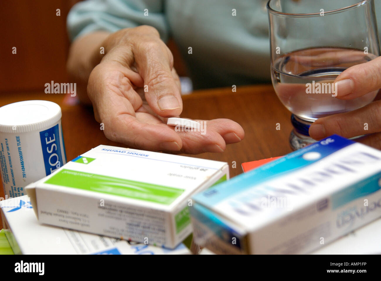 Le mani di una donna anziana tenendo una pillola e un bicchiere d'acqua circondato da scatole di lei la prescrizione di farmaci Foto Stock