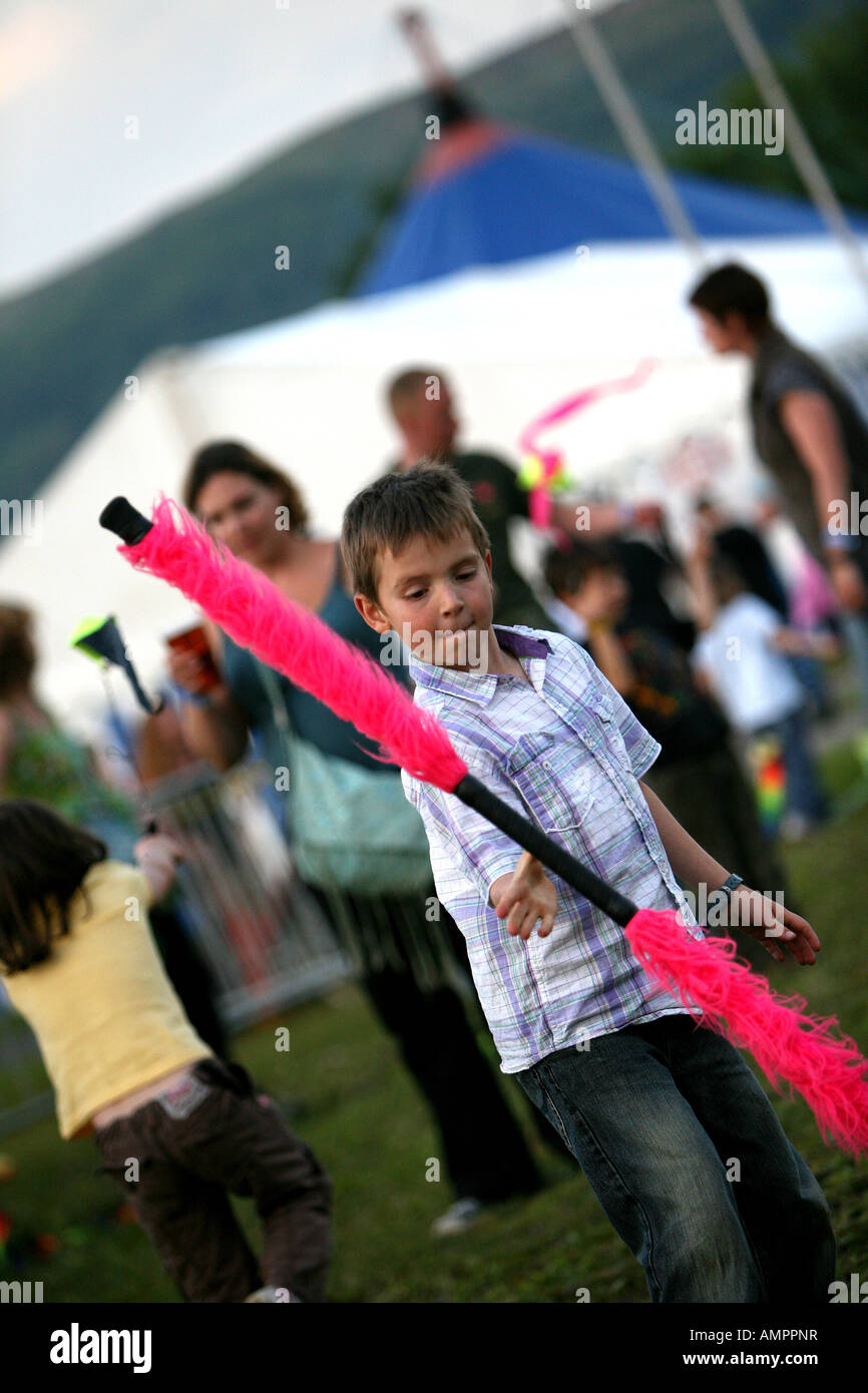 Giovane ragazzo giocando con bastoni di giocoleria al festival con curiosi in background Foto Stock
