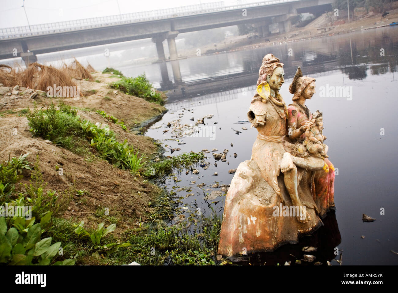 Una icona religiosa di Shiva Parvati e Ganesh semi sommersa sulle rive del fiume Yamuna a Delhi Foto Stock