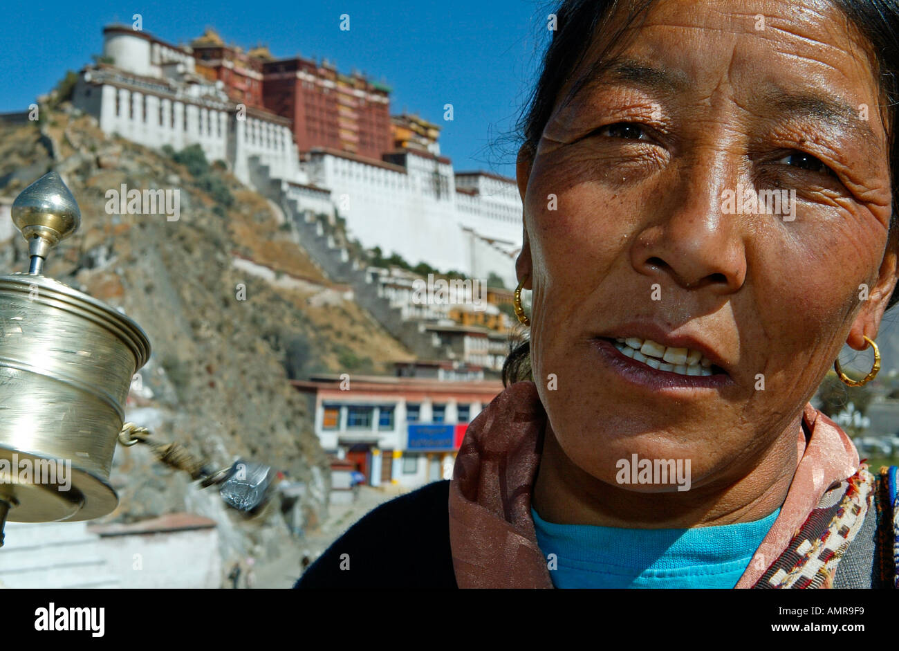 La donna gira la ruota di preghiera da palazzo del Potala del diciassettesimo secolo Dalai Lama residenza invernale Lhasa Tibet Foto Stock