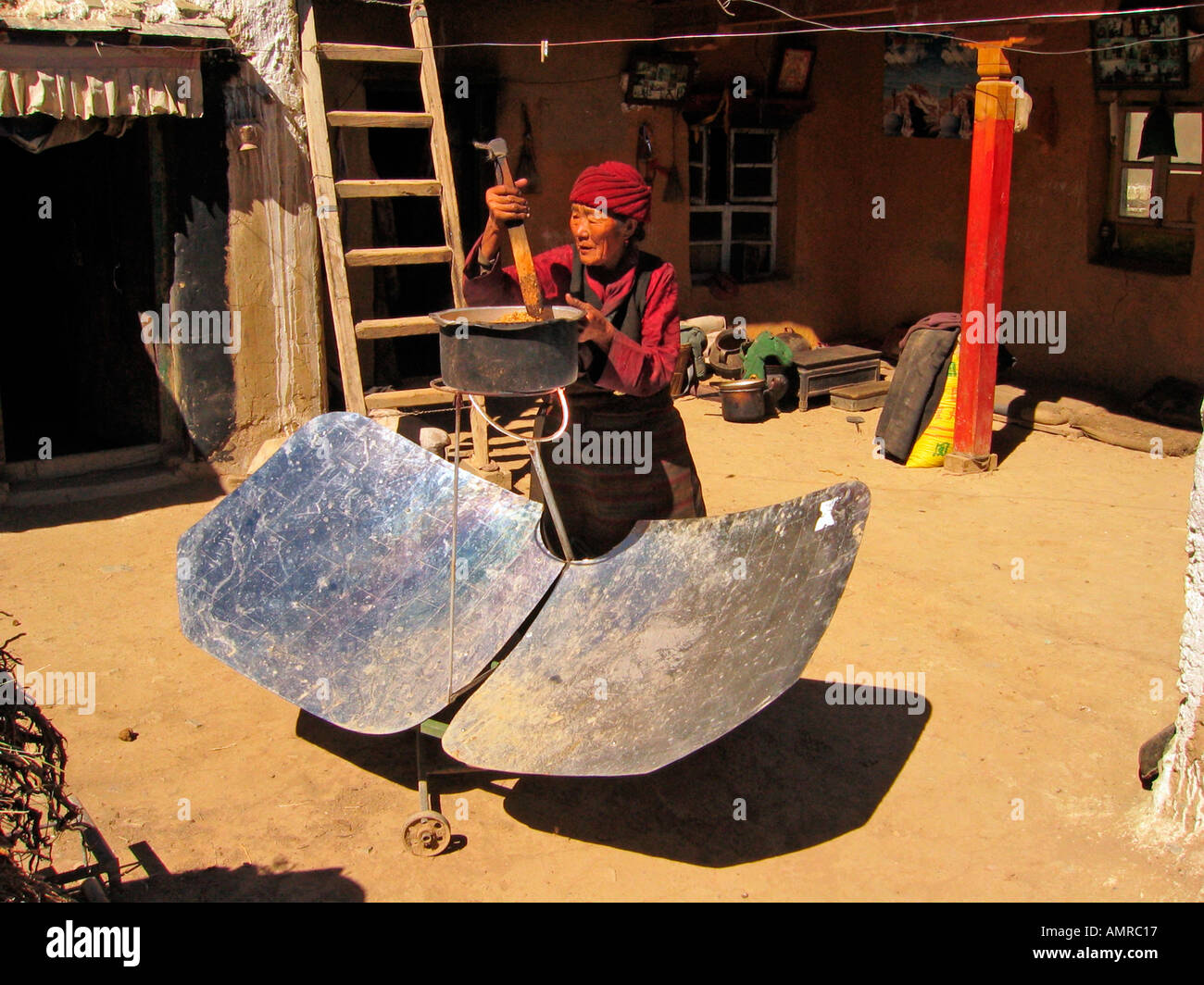 Donna suscita pot di birra d'orzo mash su pannello solare riscaldatore Lhatse Shekor Tibet Foto Stock
