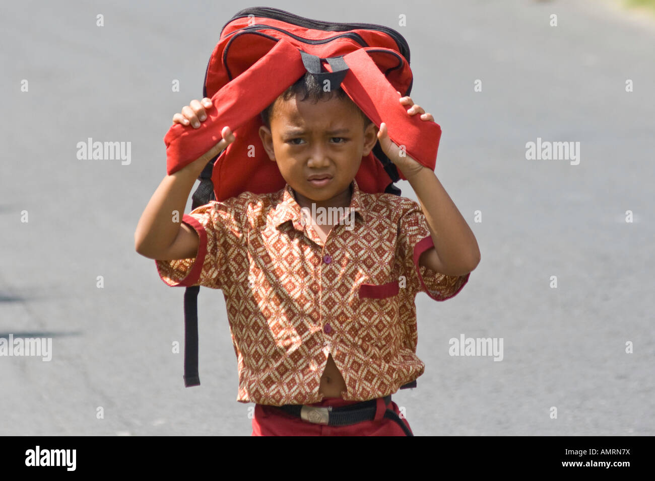 Giovane ragazzo Balinese bloccando il sole con la sua borsa sul suo modo di scuola Ubud Bali Indonesia Foto Stock