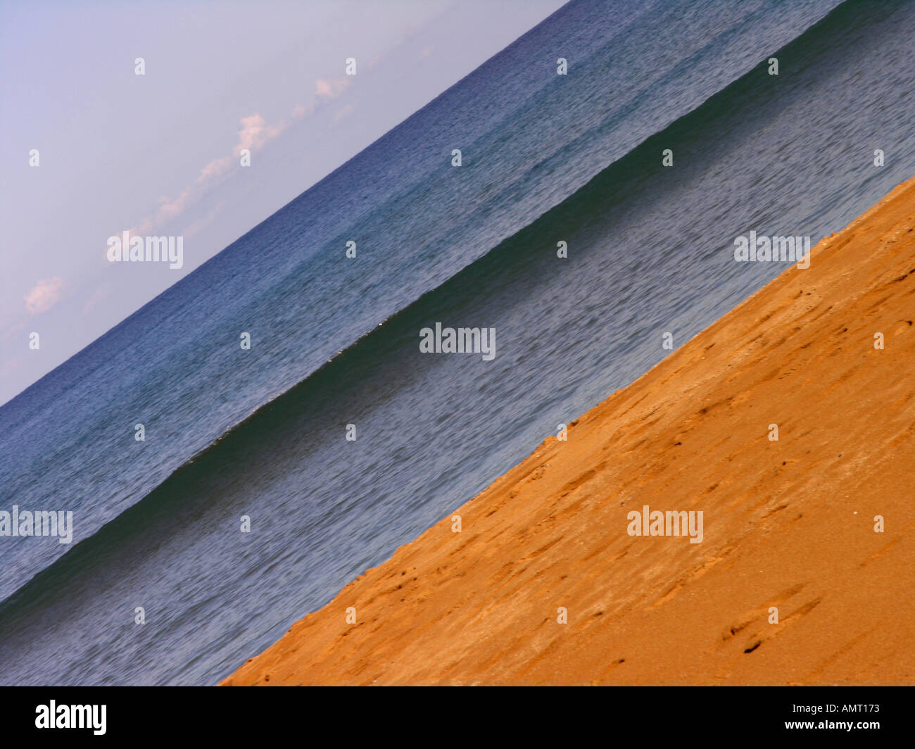 Diagonale inclinata shot spiaggia di sabbia rossa di una singola onda blu formando sotto un cielo privo di nuvole Foto Stock