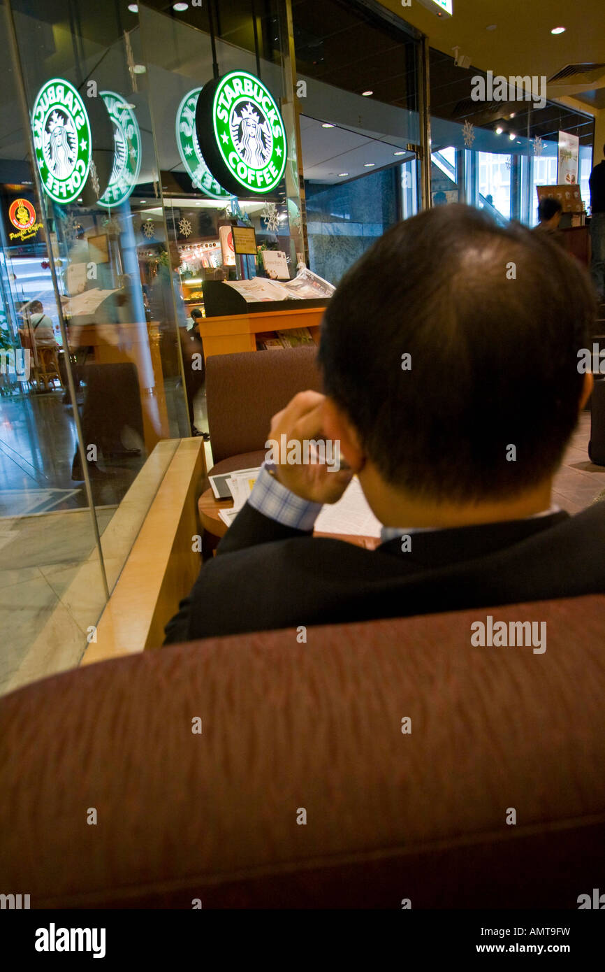 Uomo asiatico sul telefono cellulare all'interno del caffè Starbucks Cafe Hong Kong Asia Foto Stock